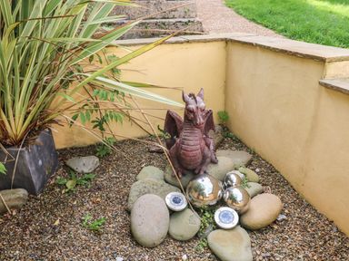 A garden corner with a small dragon statue surrounded by stones and metallic spheres at Greengate in Tenby