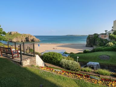 A beach with sandy shore and blue water viewed from a garden with flowers bushes and benches at Greengate in Tenby