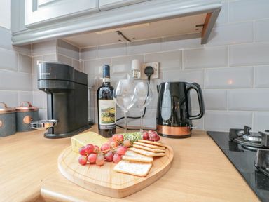 A kitchen countertop with a coffee machine kettle wine bottle wine glasses cheese grapes and crackers at Rosemary Cottage Briggswath near Sleights