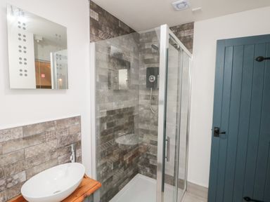 A bathroom with a glass shower enclosure a white basin on a wooden countertop a mirror and a blue door at Rosemary Cottage in Briggswath near Sleights