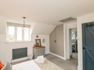A bedroom with a bed folded towels a small dresser with a mirror built in closet a window and a blue door at Rosemary Cottage in Briggswath near Sleights