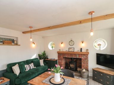 A living room with a green sofa a brick fireplace a wooden table and a television at Rosemary Cottage in Briggswath near Sleights