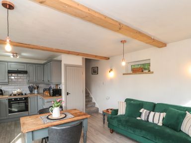A kitchen and living area with a green sofa wooden table with flowers and wooden ceiling beams at Rosemary Cottage in Briggswath near Sleights