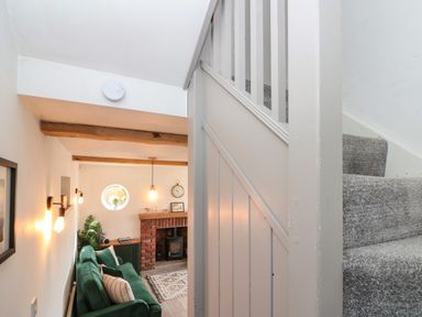 A living room with a green sofa a brick fireplace wooden beams and a staircase with grey carpet at Rosemary Cottage in Briggswath near Sleights