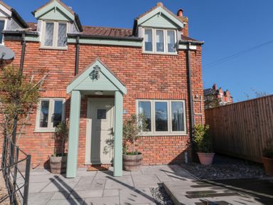 A brick house with a light green door and porch and several potted plants outside at Rosemary Cottage in Briggswath near Sleights