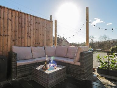 An outdoor seating area with a wicker sectional sofa and a matching table with drinks on a deck at Rosemary Cottage in Briggswath near Sleights