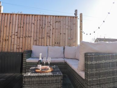 An outdoor seating area with a wicker sofa and a table with a bottle and glasses at Rosemary Cottage in Briggswath near Sleights