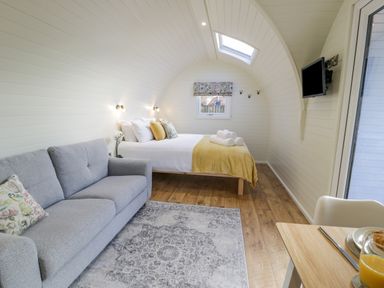 A bedroom with a bed and folded towels a grey sofa a patterned rug a wall-mounted TV and a dining table at Y Dderwen in Bontuchel near Ruthin