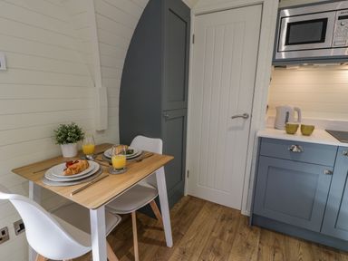 A small dining area with a wooden table set for two near a kitchen with blue cabinets and a microwave at Y Dderwen in Bontuchel near Ruthin