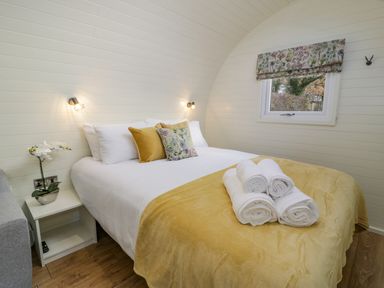A bedroom with a bed with rolled towels and floral cushions and a window at Y Dderwen in Bontuchel near Ruthin