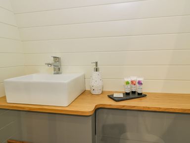 A bathroom countertop with a white square sink a soap dispenser and toiletry items at Y Dderwen in Bontuchel near Ruthin