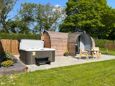 A wooden pod with outdoor hot tub and patio furniture in a garden at Y Dderwen Bontuchel near Ruthin