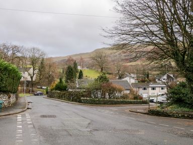 A street scene with houses trees and hills in the background at 8 Oaks Field in Ambleside