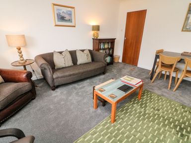 A sitting room with a grey sofa and green rug a wooden table and chairs at 8 Oaks Field Ambleside