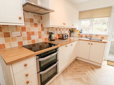 A kitchen with wooden countertops, white cabinets, tiled backsplash, and appliances at 8 Oaks Field in Ambleside