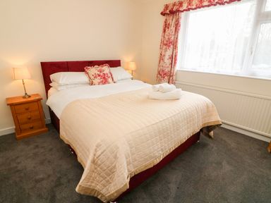 A bedroom with a bed with a beige quilt and floral curtains at 8 Oaks Field in Ambleside