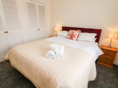 A bedroom with a double bed with beige bedspread and white towels on it with wooden bedside tables with lamps at 8 Oaks Field in Ambleside