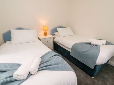 A bedroom with two single beds white linens blue throws and a nightstand with a lamp at 8 Oaks Field in Ambleside