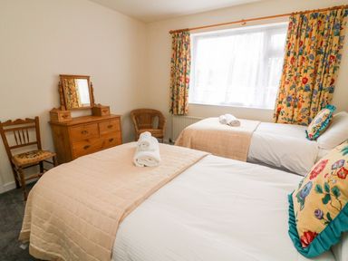 A bedroom with two beds a wooden dresser with mirror a chair and floral curtains at 8 Oaks Field Ambleside