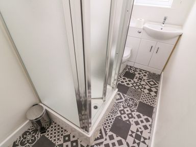 A small bathroom with a shower enclosure, a trash can, a toilet, and a sink with cabinets at 8 Oaks Field in Ambleside