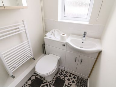 A bathroom with a toilet and sink with white cabinets white towel on cabinet and patterned floor at 8 Oaks Field in Ambleside