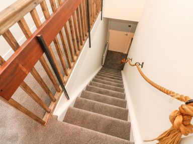 A staircase with carpeted steps a wooden railing and a rope handrail going down to a closed door at 8 Oaks Field in Ambleside