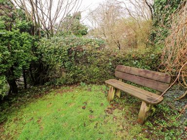 A wooden bench in a garden area surrounded by bushes and trees at 8 Oaks Field in Ambleside