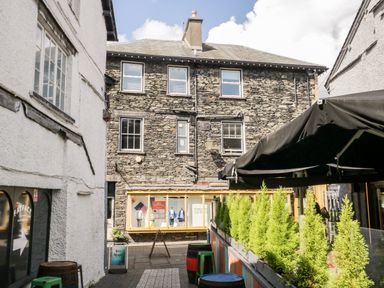 An outdoor passageway with stone buildings on both sides and small green plants on the right at Bowness Central in Bowness-On-Windermere