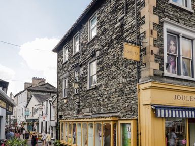A stone building with multiple windows and a yellow storefront with a Joules sign on Ash Street in Bowness-On-Windermere