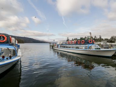 A lake with two boats docked with hills and trees in the background at Bowness Central in Bowness-On-Windermere