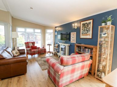 A living room with a brown sofa and red plaid armchairs next to a blue wall with framed pictures at 6 Badgers Retreat in Tunstall near Richmond