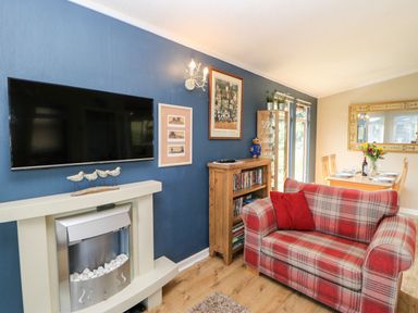 A living room with a plaid sofa a wooden cabinet a glass display unit a dining table and chairs with a large mirror at 6 Badgers Retreat in Tunstall near Richmond