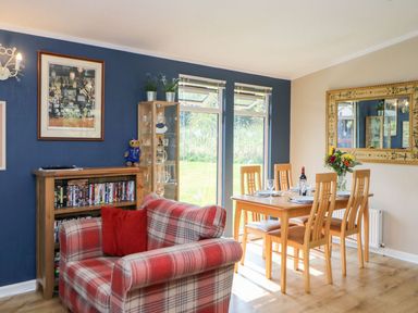 A dining room with wooden table and six chairs next to a red plaid armchair and a wooden bookshelf at 6 Badgers Retreat Tunstall near Richmond