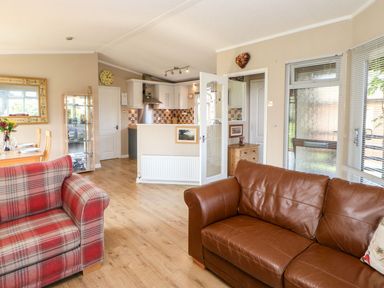 A living room with a brown leather sofa and a red plaid armchair with an open door leading to a kitchen at 6 Badgers Retreat Tunstall near Richmond