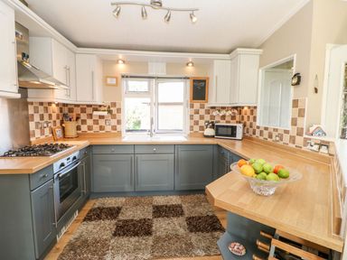 A kitchen with blue lower cabinets wooden countertops a gas stove microwave kettle a rug and a bowl of fruit at 6 Badgers Retreat Tunstall near Richmond