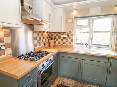 A kitchen with a gas stove oven wooden countertops a sink under a window and blue cabinets at 6 Badgers Retreat in Tunstall near Richmond