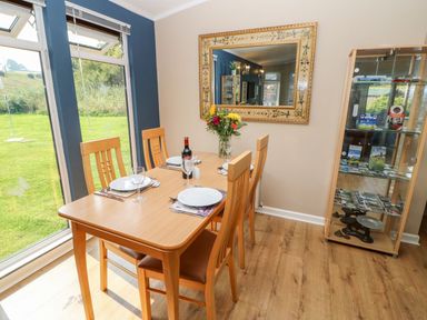 A dining area with a wooden table set for four people next to large windows a mirror on the wall and a glass display cabinet at 6 Badgers Retreat Tunstall near Richmond