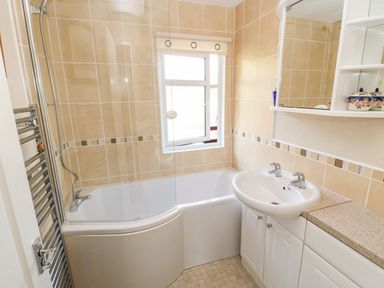 A bathroom with a bathtub shower combination a white sink and cabinet a window and a mirrored medicine cabinet at 6 Badgers Retreat Tunstall near Richmond