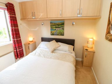 A bedroom with a double bed bedside tables lamps wall cabinets and red curtains at 6 Badgers Retreat in Tunstall near Richmond