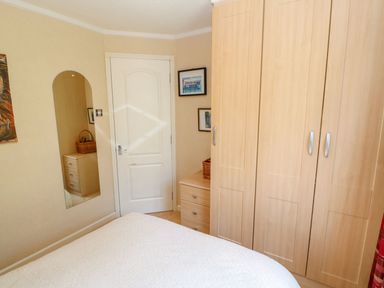 A bedroom with a white door light wood wardrobes and a bed with a white patterned cover at 6 Badgers Retreat Tunstall near Richmond