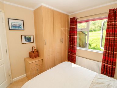 A bedroom with a wooden wardrobe a small chest of drawers and a window with red curtains at 6 Badgers Retreat Tunstall near Richmond