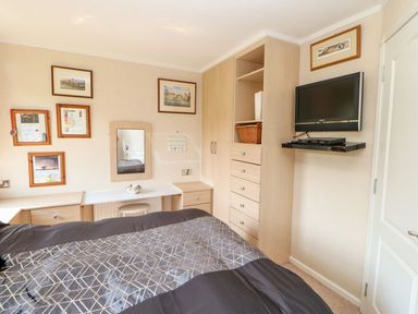 A bedroom with a bed a wall-mounted television framed pictures and built-in wooden wardrobes at 6 Badgers Retreat Tunstall near Richmond