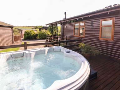 An outdoor hot tub on a wooden deck next to a wooden cabin with windows and potted plants at 6 Badgers Retreat in Tunstall near Richmond