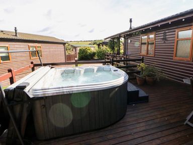 An outdoor hot tub on a wooden deck between two brown wooden cabins at 6 Badgers Retreat in Tunstall near Richmond