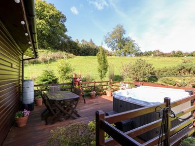 A wooden deck with a table and chairs a hot tub and potted plants overlooking a grassy hill at 6 Badgers Retreat in Tunstall near Richmond