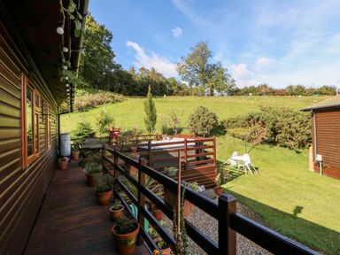 A wooden deck with potted plants and railing overlooking a grassy yard with outdoor seating at 6 Badgers Retreat in Tunstall near Richmond