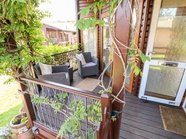 A wooden porch with two wicker chairs with cushions and plants climbing the railing at 6 Badgers Retreat Tunstall near Richmond