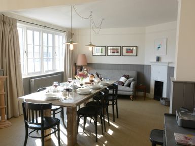 A dining room with a wooden table set with plates glasses and wine surrounded by black chairs and a gray sofa at 2 The Dunes Thorpeness