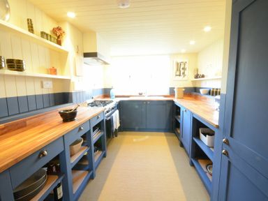A kitchen with blue cabinets wooden countertops open shelves and a stove at 2 The Dunes Thorpeness