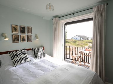 A bedroom with a bed and patterned pillows next to a balcony with a table and chairs at 2 The Dunes Thorpeness